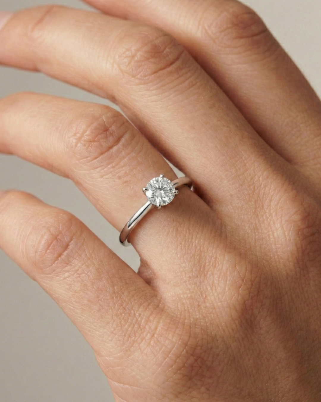 A classic round brilliant cut solitaire diamond engagement ring on a slender white gold band, styled on a hand to showcase Amorati&rsquo;s timeless bridal elegance.